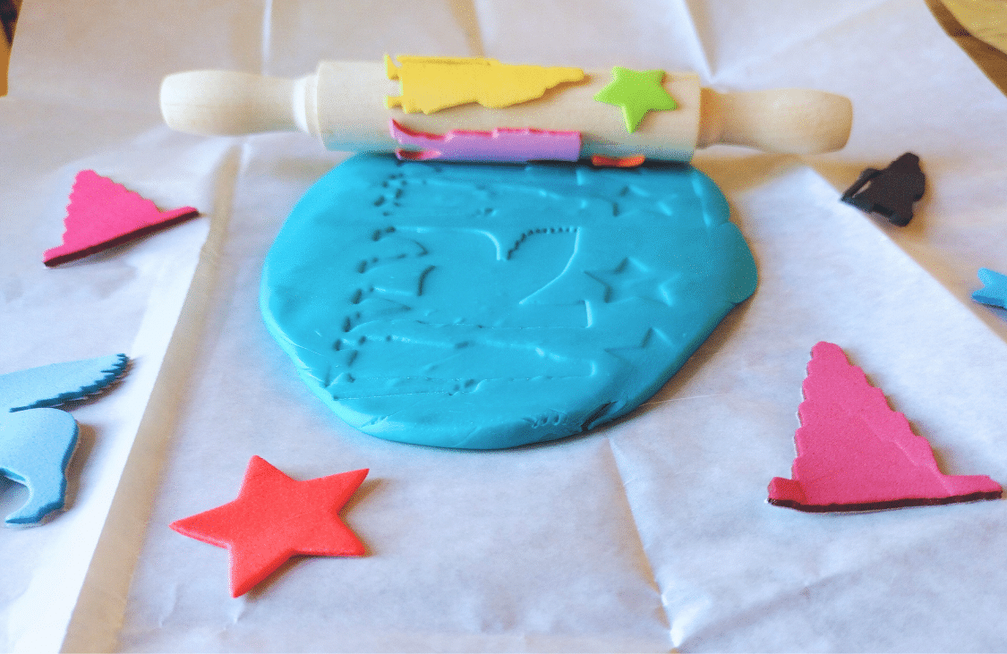 Cylinder seal craft with a decorated wooden roller making impressions in blue modelling dough